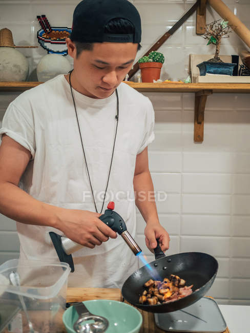 Konzentrierter junger Mann braten in asiatischem Restaurant Zutaten für japanisches Gericht namens Ramen — Stockfoto
