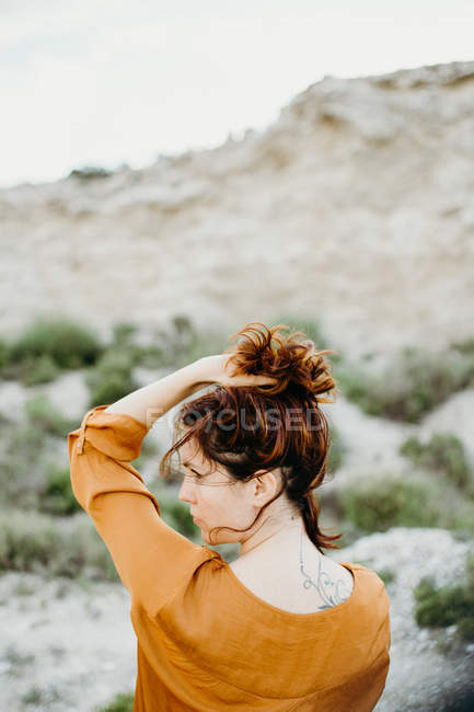 Mulher pensativa em blusa com a mão no cabelo no fundo da paisagem selvagem do deserto — Fotografia de Stock