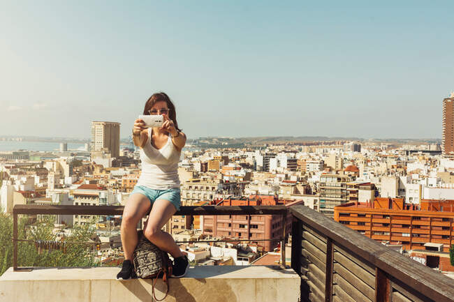 Femme sur le balcon prenant des photos vue sur la ville d'en haut — Photo de stock