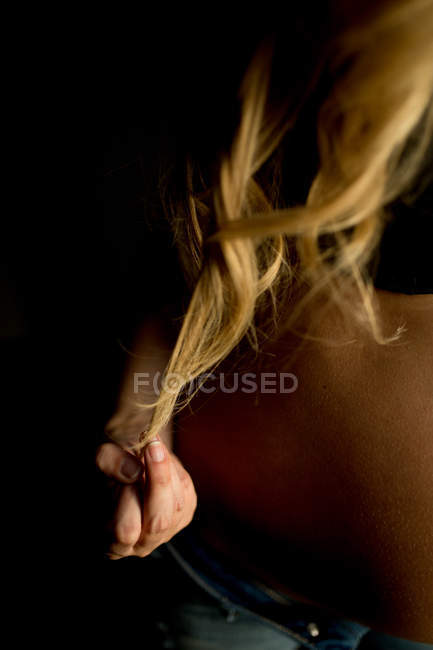 Primer plano de la mano femenina tocando el pelo rubio en la oscuridad - foto de stock