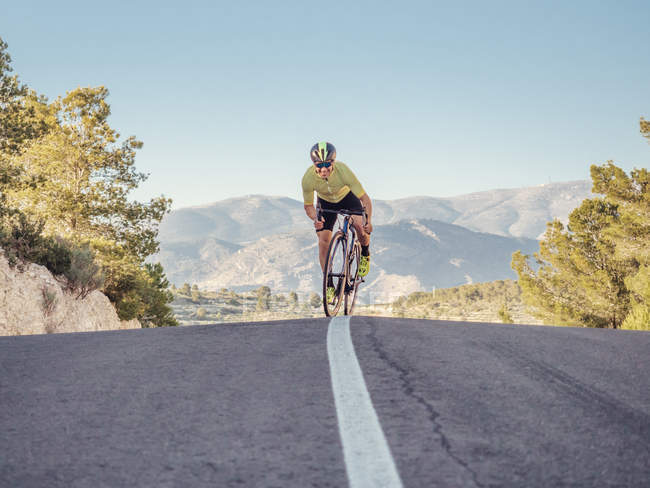 Здоровий чоловік їде на велосипеді на гірській дорозі в сонячний день — стокове фото