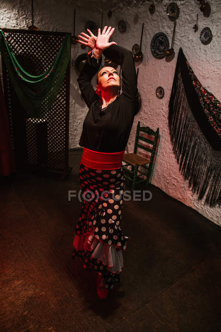 Bailarina femenina inspirada en falda de flamenco brillante realizando postura de baile en habitación étnica con objetos antiguos en la pared - foto de stock
