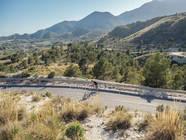 Hombre sano montar en bicicleta en carretera de montaña en un día soleado - foto de stock