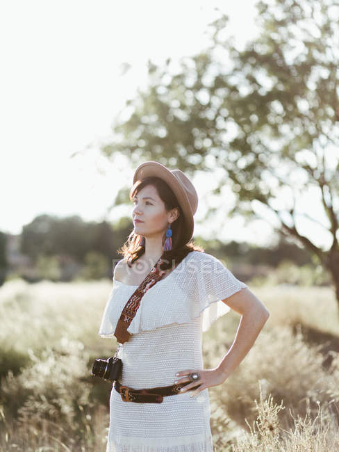 Portrait of woman in white clothes and hat standing outdoors in daylight with camera — Stock Photo