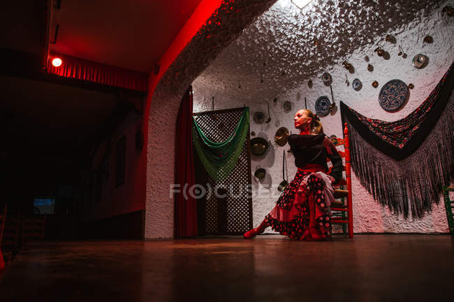 Female dancer in flamenco costume sitting in dance posture in ethnic room with antique items on wall — Stock Photo