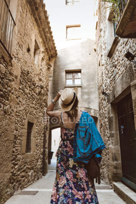 Вид ззаду на невпізнавану жінку в сукні і капелюсі, що йде по вулиці середньовічного міста — стокове фото