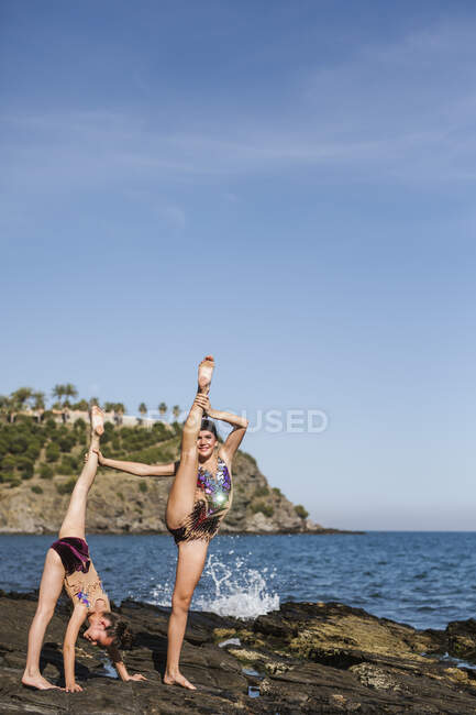 Гнучкі жінки в купальниках проводять акробатичні вправи разом на скелястому пляжі в літній час — стокове фото