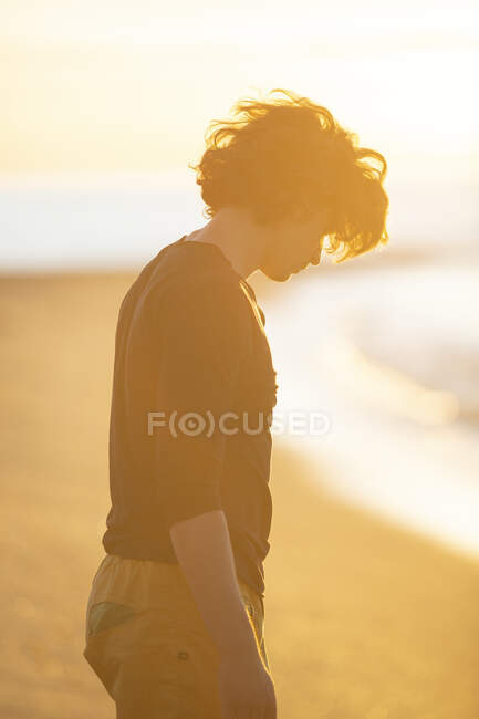 Ragazzo premuroso che cammina sulla spiaggia di sabbia alla sera del tramonto — Foto stock