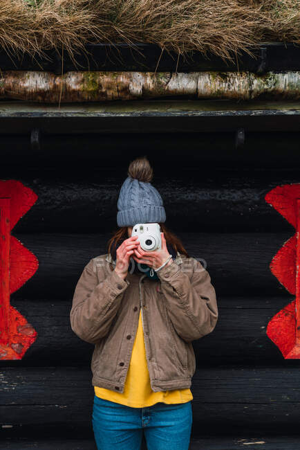 Femme portant des vêtements d'hiver devant une cabine en bois prenant des photos — Photo de stock