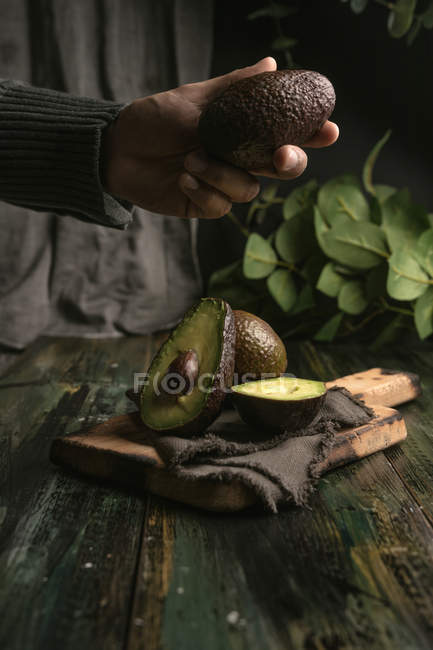 Menschenhand hält Avocado über Holztisch — Stockfoto