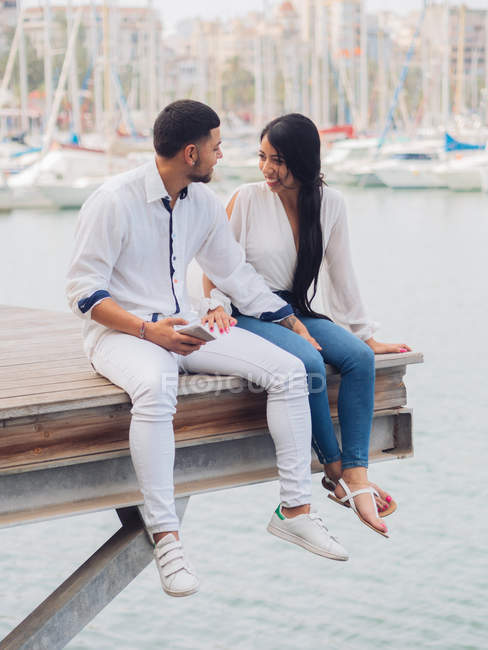 Young lovely couple sitting on dock with feet and embracing looking at each other — Stock Photo