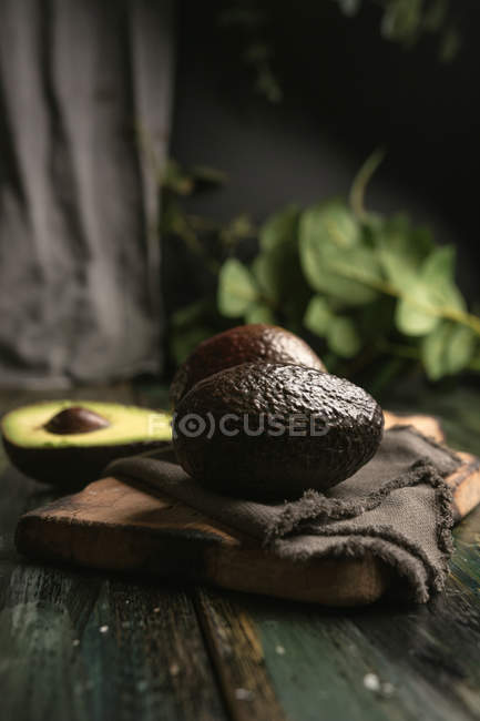 Avocado fresco intero e dimezzato su tavolo in legno rustico — Foto stock