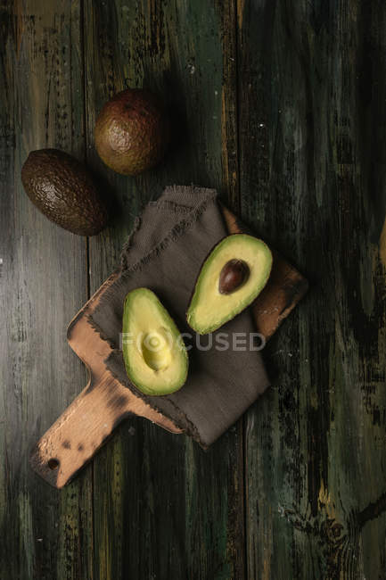 Свежие целые и наполовину авокадо на деревянном столе — стоковое фото