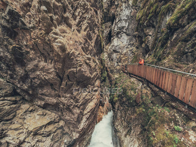 Турист, любующийся величественным видом на Альпы во время прогулки по пешеходному мосту в Доломитовых Альпах, Италия — стоковое фото