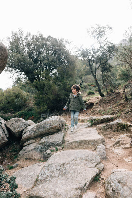Little curious kid in coat walking down rocky hillside exploring nature — Stock Photo