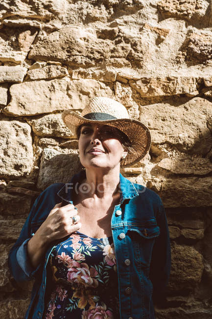 Frau mit Strohhut lehnt an Steinmauer auf Straße eines mittelalterlichen Dorfes — Stockfoto