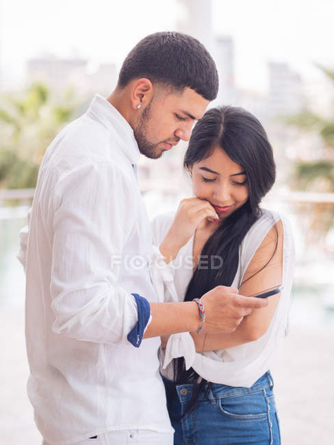 Young attractive couple in white clothes texting on mobile phone — Stock Photo