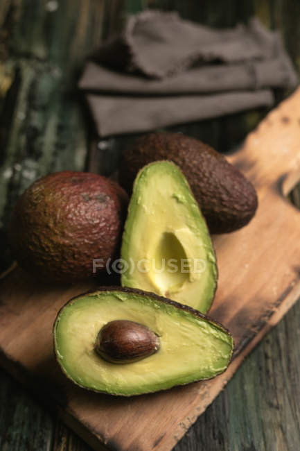 Fresh whole and halved avocados on wooden board — Stock Photo