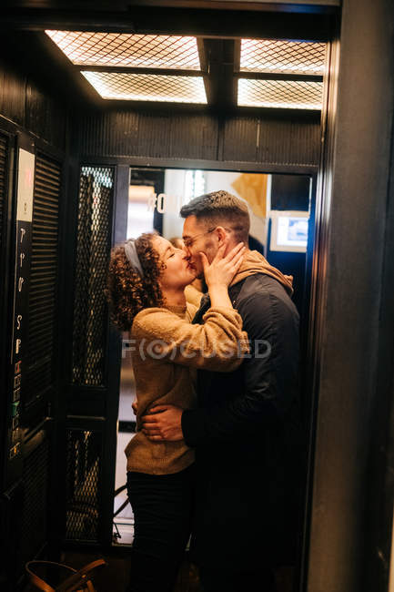 Vista lateral de alegre joven hombre y mujer sosteniendo la puerta del ascensor y sonriendo durante la cita romántica - foto de stock