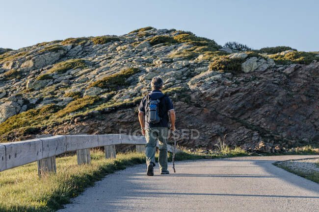 Back view of a senior man with back pack and wooden stick hiking through the mountain — Stock Photo