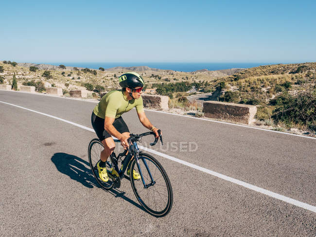 Здоровый человек катается на велосипеде по горной прибрежной дороге в солнечный день — стоковое фото