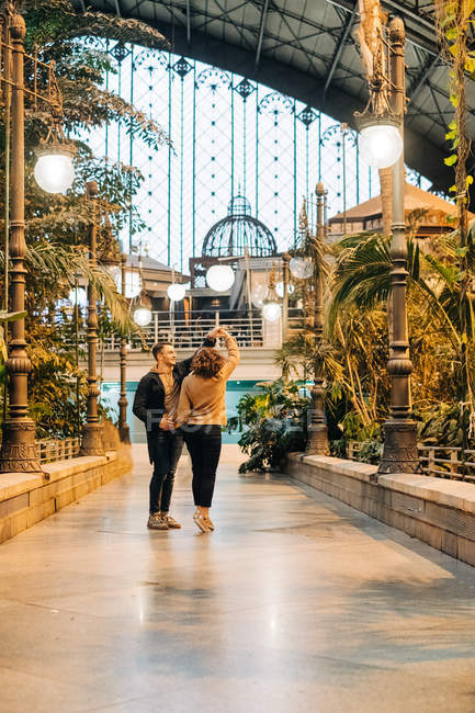 Веселые юноша и девушка обнимаются и танцуют, стоя внутри освещенного павильона во время свидания — стоковое фото