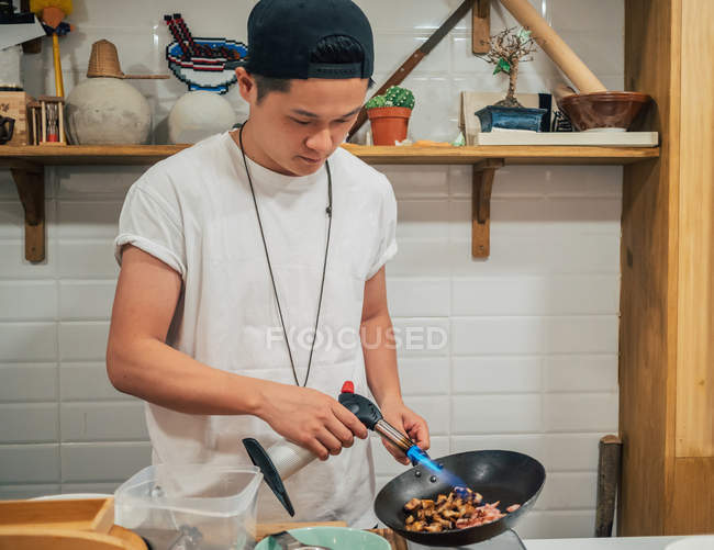 Concentré jeune homme friture ingrédients pour plat japonais appelé ramen dans le restaurant asiatique — Photo de stock