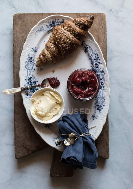 Crujiente croissant y mermelada de mantequilla y fresa servido en plato sobre tabla de madera - foto de stock