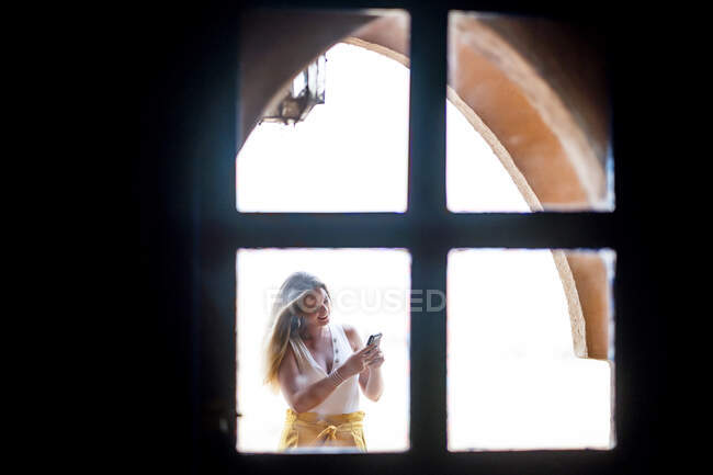 Mujer feliz usando teléfono móvil cerca del paisaje del desierto de pie en el balcón de piedra, Marruecos - foto de stock