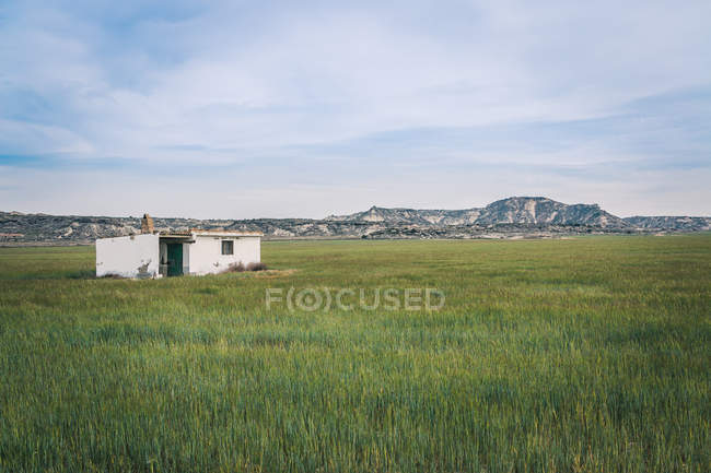 Краєвид білого самотнього будинку в нескінченно зелених полях на тлі пагорбів і блакитного неба — стокове фото