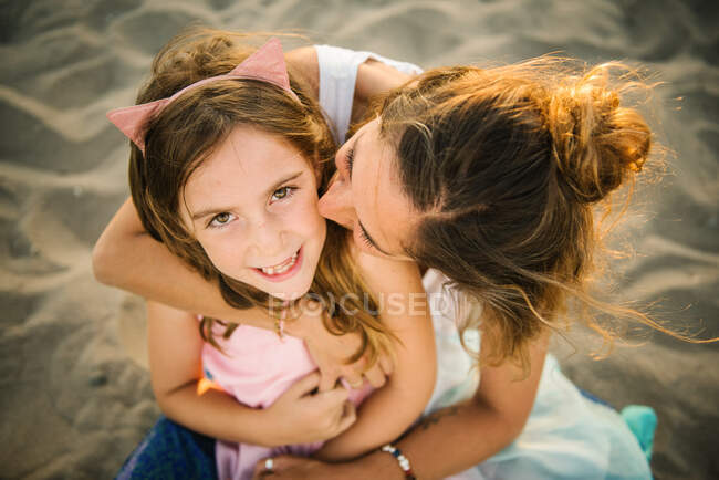 Vista dall'alto della donna adulta baciare bella ragazza abbracciando con amore sulla spiaggia di sabbia in luce del tramonto — Foto stock