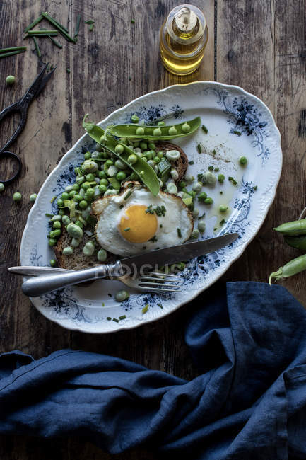 Подається тарілка з зеленим горохом і смаженим яйцем на дерев'яному столі — стокове фото