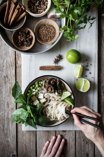Human hand with chopsticks and Pho soup with noodles on marble board on wooden table with spices — Stock Photo