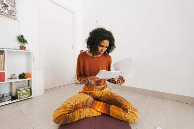 Афроамериканская привлекательная молодая женщина сидит со скрещенными ногами и проверяет бумагу — стоковое фото