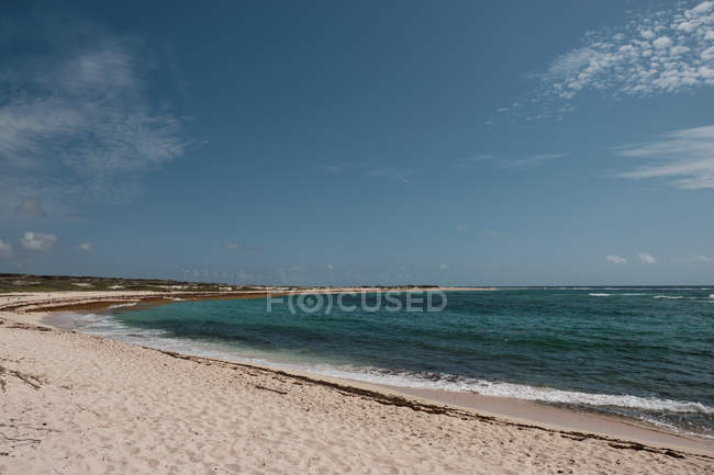 Incredibile spiaggia di sabbia e oceano calmo con onde di schiuma sullo sfondo del cielo nuvoloso — Foto stock
