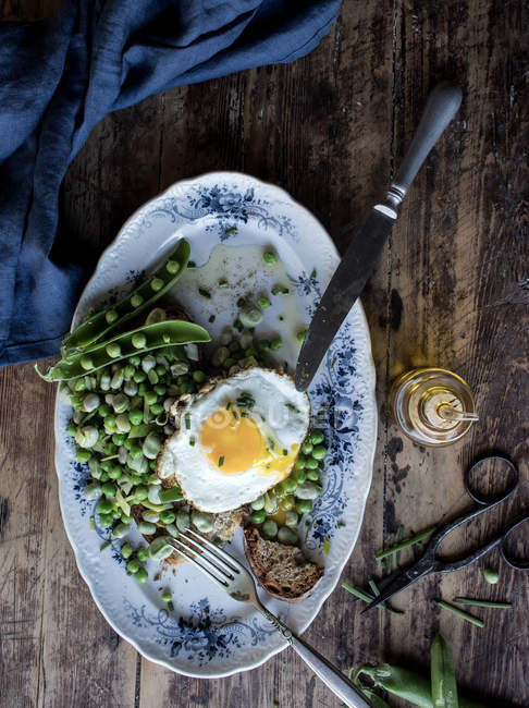 Served plate with sauteed green peas and fried egg on wooden table — Stock Photo