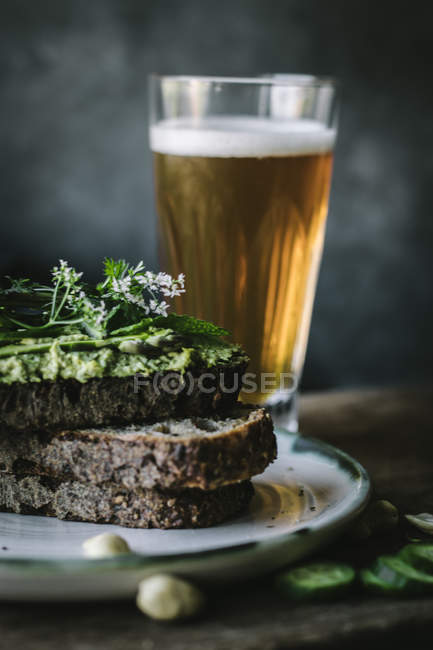 Toasts mit grüner Cashewpastete, Kräutern und Gurkenscheiben mit einem Glas Bier auf Holzbrett — Stockfoto