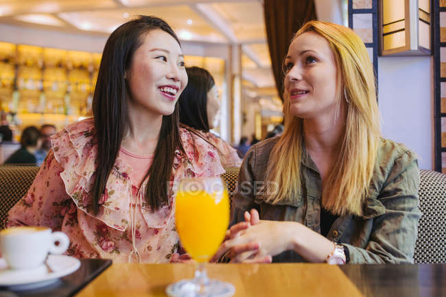 Молодые многорасовые женщины улыбаются и разговаривают друг с другом, сидя за столом в уютном кафе — стоковое фото