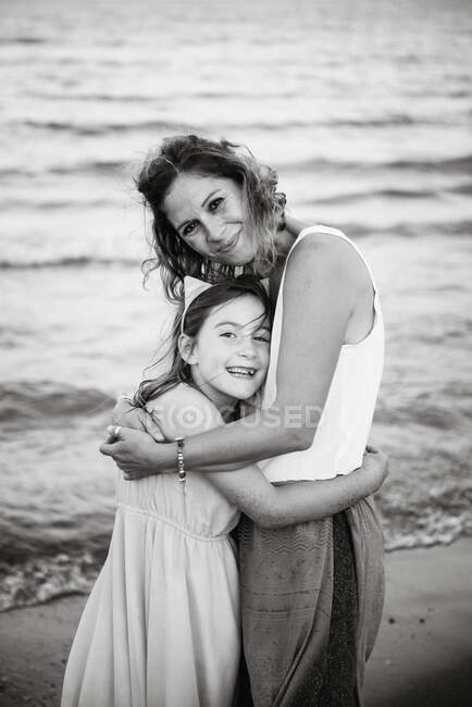 Black and white of smiling adult woman with charming girl embracing and looking at camera — Stock Photo