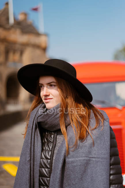 Donna rossa che passa attraverso un furgone di colore rosso retrò sul ciglio della strada con castello di pietra invecchiato sullo sfondo, Scozia — Foto stock