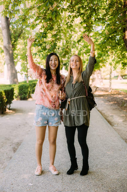 Захоплені багаторасові жінки вказують і махають руками, стоячи на парковій алеї в сонячний день — стокове фото