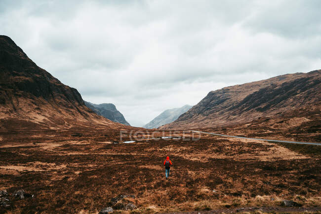 Неузнаваемый человек в красном пальто прогуливается по живописным горам Шотландии — стоковое фото
