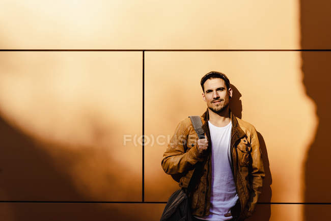 Uomo positivo in abito elegante guardando la fotocamera mentre si appoggia sulla parete dell'edificio moderno nella giornata di sole — Foto stock