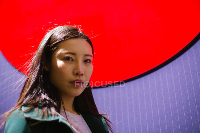 Portrait of serious Asian woman standing near bright wall on city street — Stock Photo