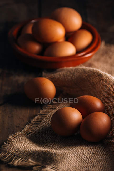 Huevos de pollo con tazón y saco sobre mesa de madera - foto de stock