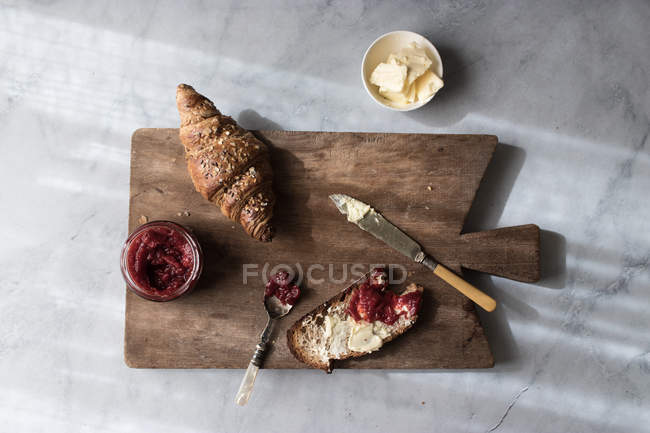 Knuspriges Croissant und Toast mit Butter und Erdbeermarmelade auf Holzbrett serviert — Stockfoto