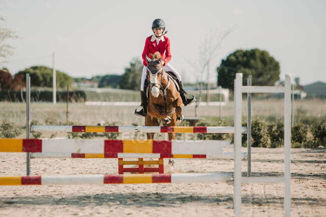 Fantino adolescente su cavallo che salta su barre di legno orizzontali mentre cavalca su pista — Foto stock