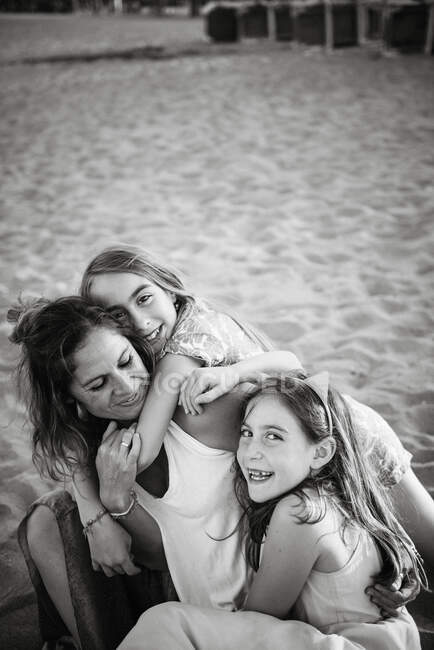From above view of woman with playful daughters lying on sandy beach having fun together, black and white photo — Stock Photo
