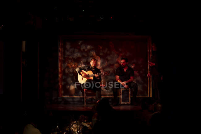 Hispanic men playing percussion and acoustic guitar during flamenco performance on dark stage — Stock Photo
