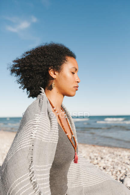 African American young woman meditating in lotus yoga posture on sandy beach in bright day — Stock Photo